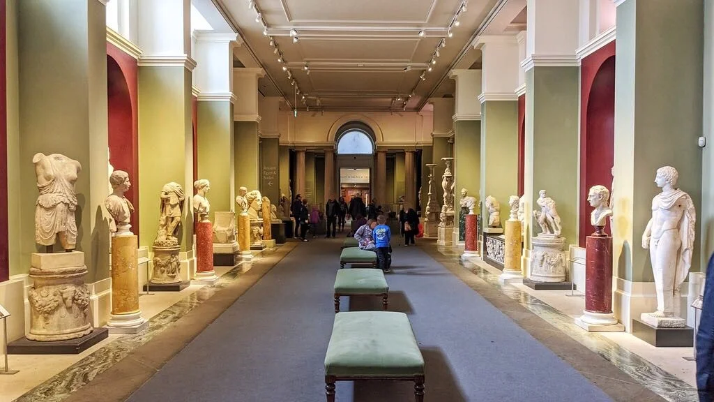 Museum gallery lines with white statues on both sides, with benches in the middle. The White Lie: Questioning the Legacy of ‘Whitewashing’ Ancient Sculpture