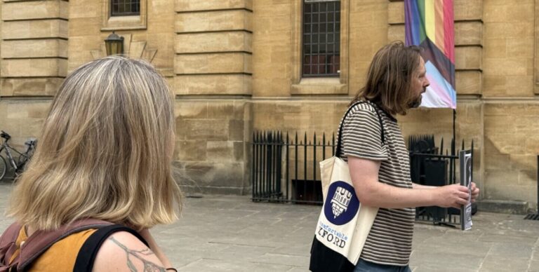A guide holds up a photo to show a group of people on the Power, Women, and Queer History tour of Oxford