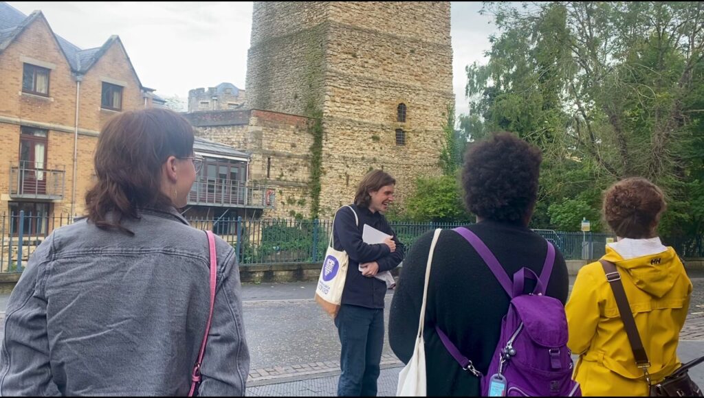 A group of tour attendees stand in front of an Uncomfortable Oxford guide and learn about medieval history in Oxford.