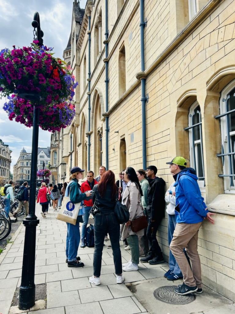 A group of tour attendees stand in front of an Uncomfortable Oxford guide and learn about medieval history in Oxford.
