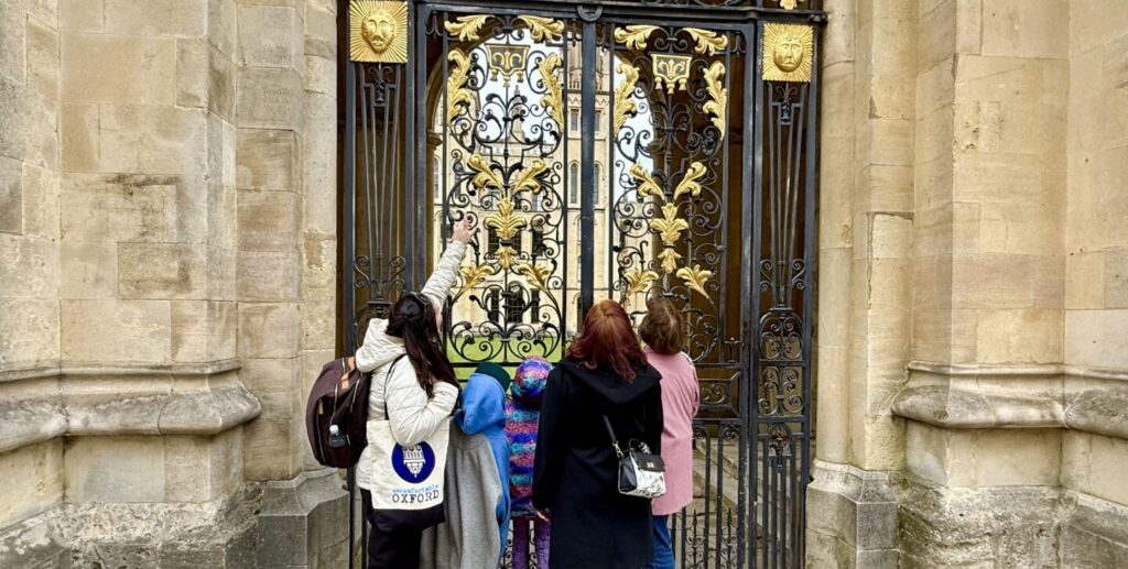 A group of children and tourists look up at the golden gates of All Souls College on a tour of Oxford's medieval history.