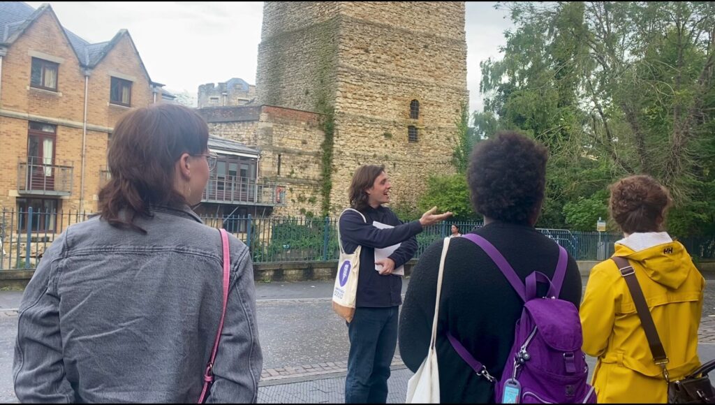 A group of tour attendees stand in front of an Uncomfortable Oxford guide and learn about medieval history in Oxford.