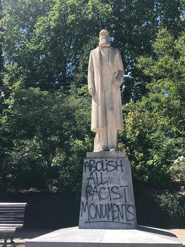 Statue of a bearded man in a park with graffiti on the base.