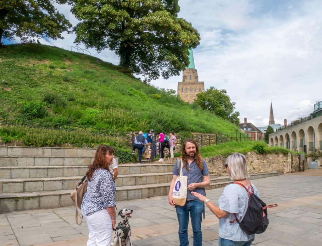 A group of attendees stand outside Oxford castles and listen to an Uncomfortable Oxford guide.