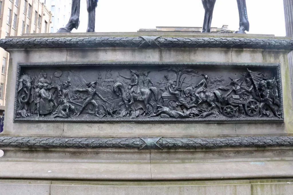 Battle scene engraved on a bronze plinth at the base of a statue.
