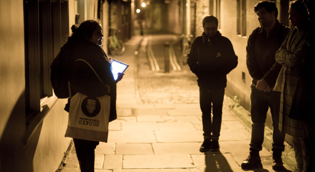 An Uncomfortable Oxford ghost tour guide stands telling a ghost story in the twilight to a tour group