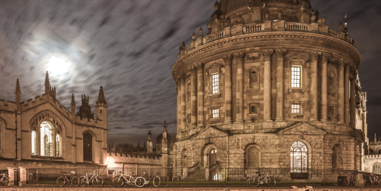 A dark and cloudy night in front of the Radcliffe Camera Library with a ghostly moon in the background.