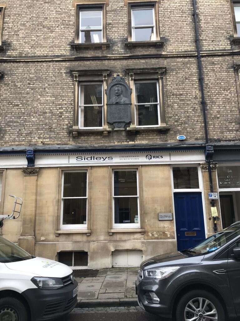 Street side building façade showing 3 floors, featuring a memorial plaque on the first floor.