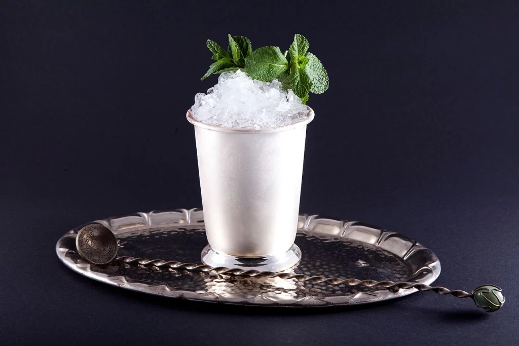 Stock image of a cocktail on a silver tray, topped with shaved ice and mint leaves.