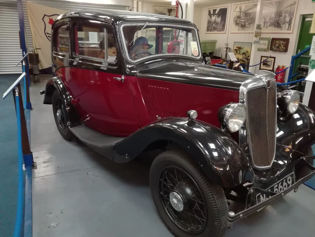 Photo of an early twentieth century car in a museum display, with mannequins inside.