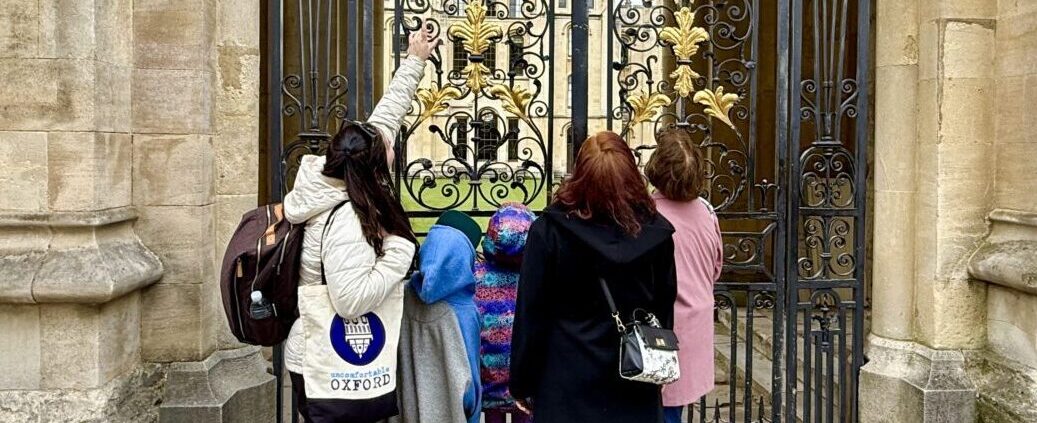 An Uncomfortable Oxford tour guide shows a detail to an onlooking audience at All Souls College.
